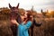 Beautiful young female elf with long dark wavy hair petting her horse resting in the woods forest nymph stroking her horse care