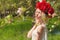 Beautiful young gentle elegant young blond woman with red peony in a wreath of white blouse walking in the lush apple orchard