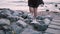 Beautiful young girl in black dress walking up on big river shore stones on summer city sunset, tilt down slow motion.