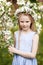 Beautiful young girl in blue dress in the garden with blosoming  apple trees. Cute girl  holding apple-tree branch