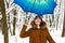 Beautiful young girl with blue umbrella in snowy forest. Snowfall concept. Woman under wet snow rain in winter park.