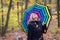 Beautiful young girl with colorful umbrella is enjoying the dropping leaves in the autumnal forest