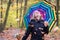 Beautiful young girl with colorful umbrella is enjoying the dropping leaves in the autumnal forest