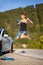 Beautiful young girl jumping next to an electric car. Holding blue charging cable