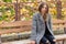 Beautiful young girl with large autumn sad eyes in a coat and ripped black jeans sitting on a bench in autumn park