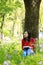 Beautiful young girl Listen to music on a mobile phone while sitting under giant oak