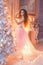 Beautiful young girl with long curly hair in a pink ball gown standing near the Christmas tree and fireplace with festive decor an