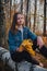 Beautiful young girl with long dark brown hair in a denim jacket sits on a log and holds yellow maple leaves in well-groomed hand