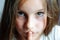 Beautiful young girl with long hair puts a finger in her mouth, close portrait