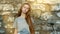 A beautiful young girl with long hair stands near a stone wall and looks at the camera