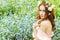 Beautiful young girl with long red hair with flowers in her hair, sitting in a field in blue flowers