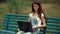 Beautiful young girl looking at a laptop while sitting on a bench