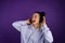 Beautiful young girl loudly singing in headphones in a sweatshirt on a purple background