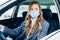 Beautiful young girl in a mask sitting in a car, protective mask against coronavirus, driver on a city street during a coronavirus