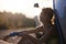 Beautiful young girl next to an electric car. Holding a charging cable. Sunset backlight