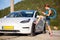 Beautiful young girl next to an electric car. Standing with a blue charging cable