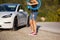 Beautiful young girl next to an electric car. Standing with a blue charging cable