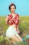 Beautiful young girl with perfect tempting smile wearing red tied up blouse, white shorts and headband sitting in the field