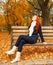 Beautiful young girl portrait sit on bench in park and relax, yellow leaves at fall season, redhead, long hair