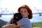 The beautiful young girl with red hair embraces on the street of the pet a black dog of breed a pug.