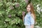 Beautiful young girl with red hair in the garden with lilac