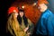 A beautiful young girl in a red helmet and with a electronic tablet in her hands is standing with a miner in a coal mine.