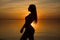 Beautiful young girl in shorts stands by the sea on a sunset background, silhouettes