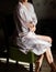 Beautiful young girl in silk robe sitting on chair and crosses.