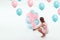 A beautiful young girl sits with blue and pink balloons on a white background. Happiness, spring, holiday