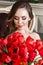 A beautiful young girl is sitting on the sofa and holding a large bouquet of red tulips. March 8 concept. Morning of the bride.