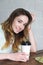 Beautiful young girl sitting at the table with coffee, head tilted and smiling looking at the camera.