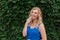 Beautiful young girl smiles in a blue dress, against a background of hedges of wild grapes. Copy space