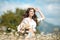 Beautiful young girl smiling with basket of flowers over chamomile field. Carefree happy brunette woman with healthy wavy hair