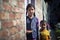 Beautiful young girl stand outside home door holding her brother.