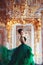 Ð beautiful young girl standing in a haute couture green dress in a luxurious gold interior.