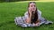 Beautiful young girl in summer dress lies on grass in park, using smartphone.