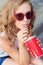 Beautiful young girl in sunglasses sitting on the street and drink a coke with a paper Cup from the tube