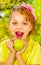 Beautiful young girl, wearing a yellow t-shirt holding a healthy apple and colorful dragees in her lips, in a blurred