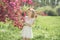 Beautiful young girl in white dress enjoying warm day in park during cherry blossom season on a nice spring