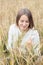 Beautiful young girl in a white sweater sits in a wheat field