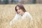 Beautiful young girl in a white sweater sits in a wheat field