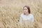 Beautiful young girl in a white sweater sits in a wheat field