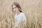 Beautiful young girl in a white sweater sits in a wheat field and looks thoughtfully at the camera