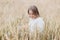 Beautiful young girl in a white sweater sits in a wheat field and smiles cheerfully