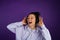 Beautiful young girl with white teeth listening to music and loudly singing in headphones in a sweatshirt on a purple