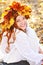 Beautiful young girl in a wreath from yellow leaves, in white clothes, sitting on fall leaves on a Sunny day and laughing