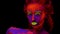 A beautiful young half-naked girl dancing with glowing paint on her body in black light. Pretty woman with glowing