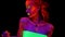 A beautiful young half-naked girl dancing with glowing paint on her body in black light. Pretty woman with glowing