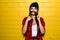 Beautiful young hipster girl posing, smiling, do fake mustache near urban yellow wall background.