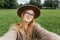 Beautiful young hipster woman taking selfie on green grass at the park. Looking at camera and smile. Travel and active